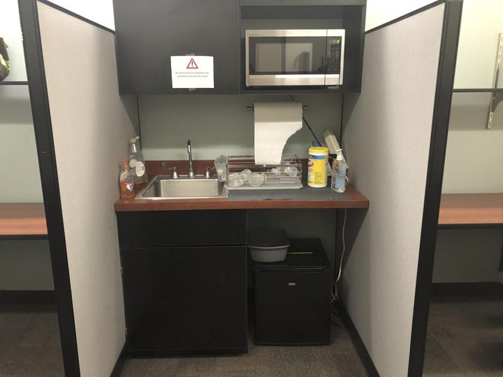 space with sink, mini fridge, microwave and cleaning supplies.